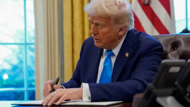 US President Donald Trump signs a document in the Oval Office at the White House