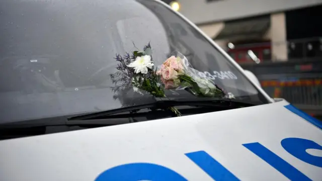 Flowers are placed on the windshield of a police vehicle following a shooting at the Risbergska School