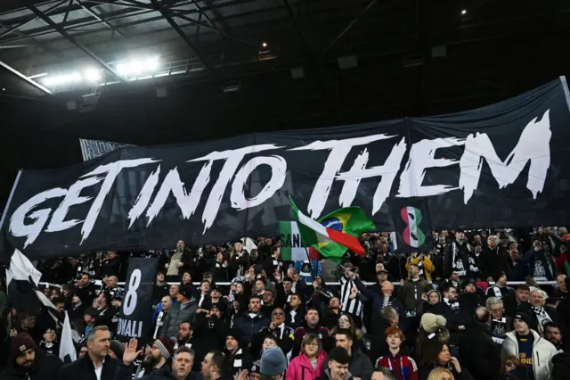 Newcastle fans hold a banner aloft that reads: Get into them