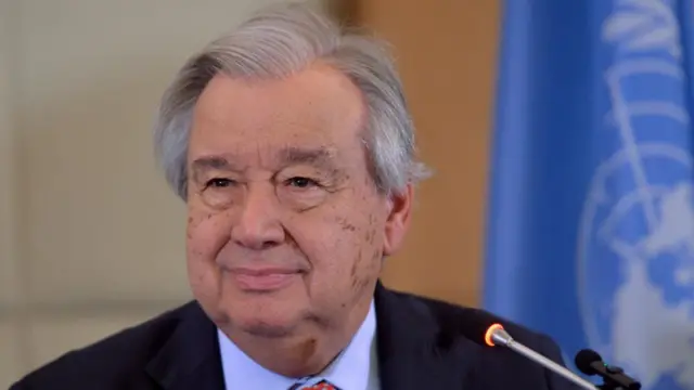 Antonio Guterres smiling towards camera sat behind a microphone