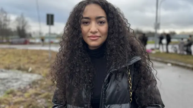 Reham Attala, 21, wears a black puffer jacket and speaks to BBC reporters