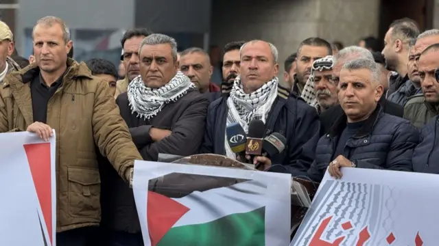 A crowd of men, looking stony faced, holding banners and posters