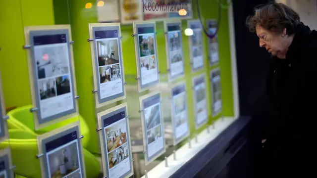 A pedestrian looks at residential property information leaflets displayed in the window of an estate agent