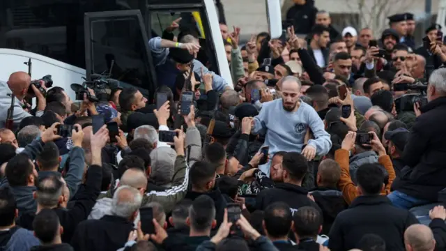 A crowd of men films people entering a bus on their phones