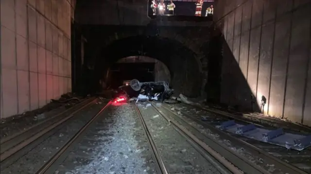 The burnt out car can be seen lying on the railway lines close to the bridge.