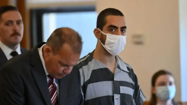 Matar wears a face mask and a striped prison jumpsuit as he stares at the camera inside a courtroom