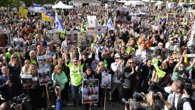 A large crowd cheering and holding banners as they watch a live stream on a big screen reporting on the release of the three Israeli hostages