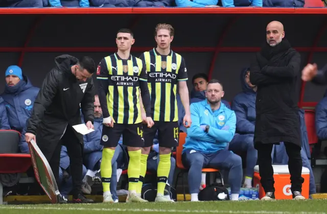 Manchester City's Phil Foden and Kevin De Bruyne wait to enter the game as manage Pep Guardiola looks on