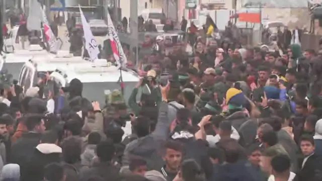 Three white vehicles with Red Cross flags make their way through a big crowd of people