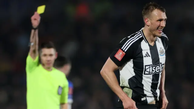 Newcastle United's Dan Burn is shown a yellow card by referee Matt Donohue