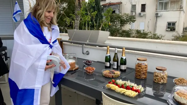 A family member draped in an Israeli flag smiles beside a table filled with champagne and cakes