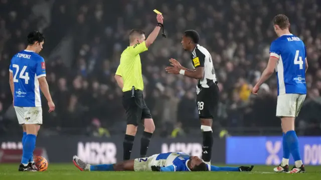 Referee Matthew Donohue shows Newcastle United's Joe Willock a yellow card