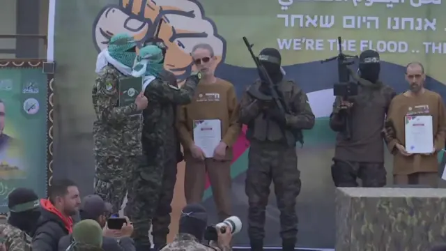 Israeli hostage speaks into microphone surrounded by Hamas fighters