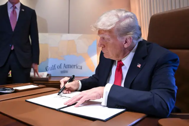 Donald Trump signs an executive order. A map is behind him, with a label saying Gulf of America