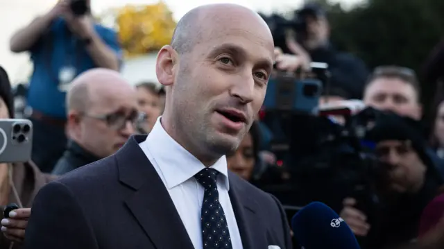 Stephen Miller in a black blazer, white shirt, and dark blue tie.