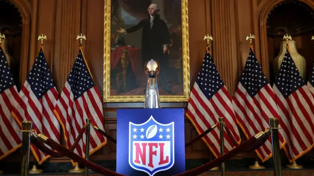 A trophy with the logo of the National football League, flanked by American flags and the George Washington painting in the background