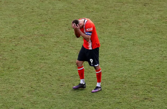 Carlton Morris stand with his head in his hands in the middle of the pitch