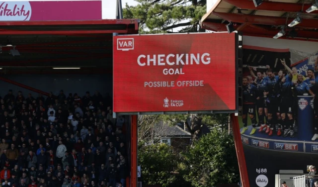 A big screen displays a VAR review message