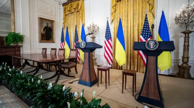 The podiums of Zelensky and Trump are left empty, with the respective flags - Ukrainian and American - draped in the background