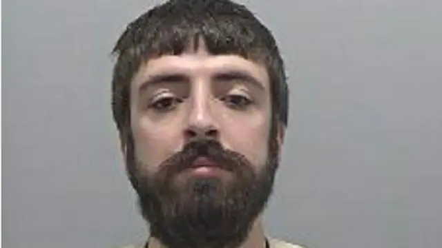 Custody mugshot of Kyle Clifford. Only his head and shoulders are visible in the picture. He has a bushy black beard and hair.