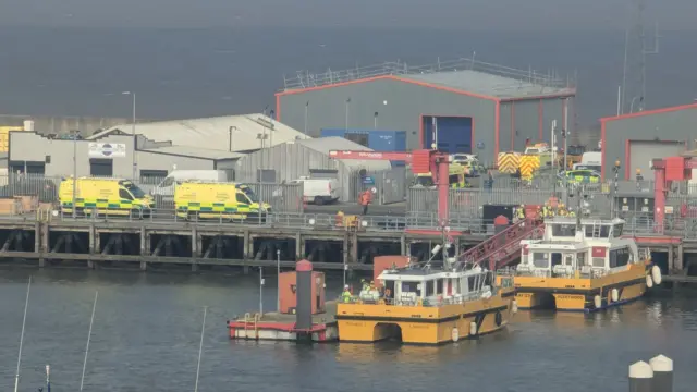 Two small rescue boats are seen arriving at the port of grimsby. two ambulances can be seen to the side.