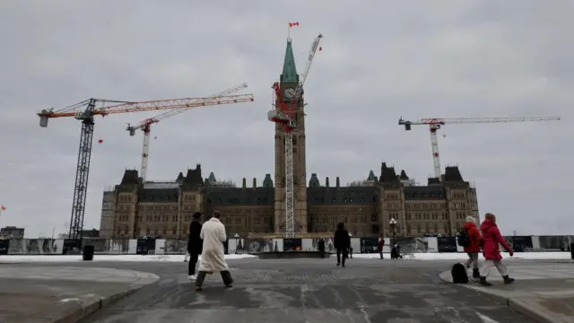 Canada's Parliament building is seen in winter time, with construction cranes around it.