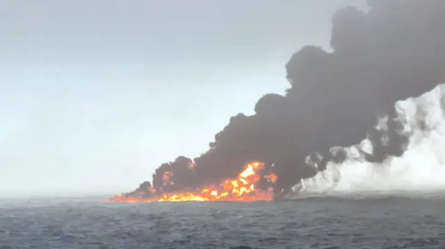 A large ball of fire on top of the grey sea, with a huge cloud of black smoke