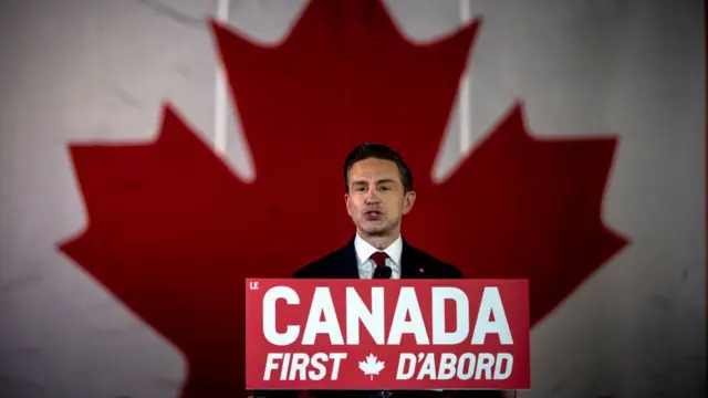 Poilievre stands in front of a sign that reads: Canada First, D'abord