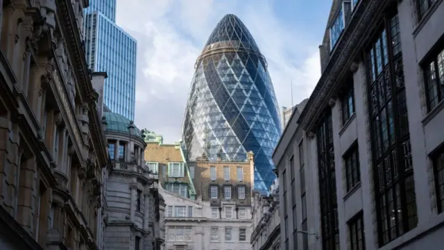 The Gherkin seen between buildings surrounding it.