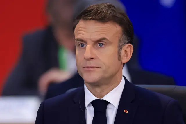 Headshot o Macron in a suit looking ahead of him with an alert expression