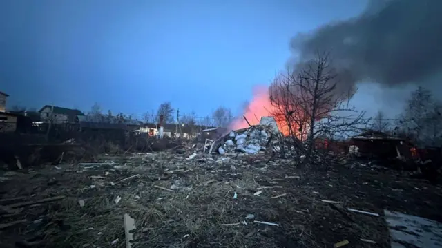 Rubble is on the ground while a fire blazes on the horizon.