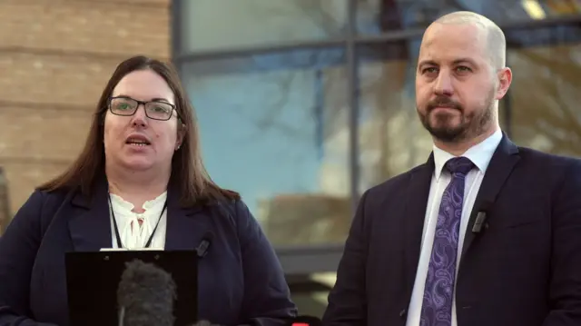 Lisa Kiff and Nick Gardner, both standing outside court. Ms Kiff is reading a statement from a clipboard while Mr Gardner watches on. Both are dressed smartly.