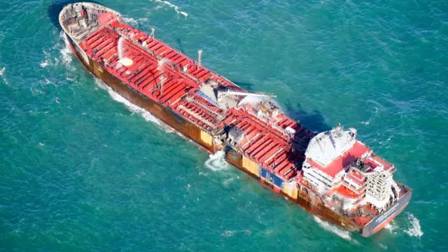 A view of the MV Stena Immaculate oil tanker with damage on the side and water pouring out.