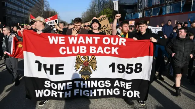 Fans, wearing black as a protest, hold up banners during a demonstration against seat prices and the current ownership of Manchester United,