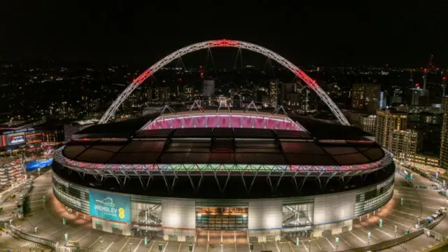 Wembley Stadium lit up at night.