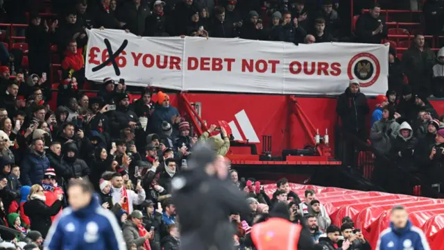 Manchester United fans display a banner that reads "£66 Your debt not ours" in protest against the clubs ownership