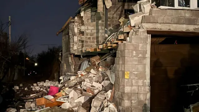 A severely damaged building with rubble everywhere and bricks strewn on the floor