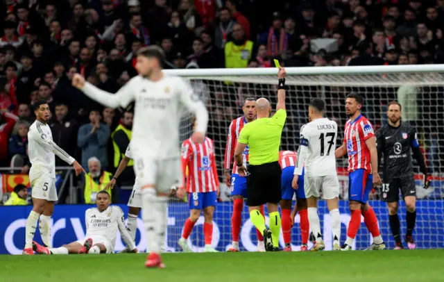 Referee Szymon Marciniak shows a yellow card to Clement Lenglet.