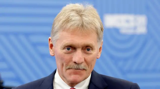 Peskov wearing a suit and tie looks at the camera