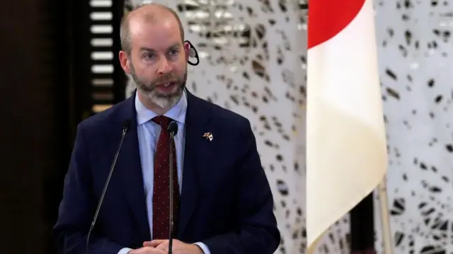 British Trade Secretary Jonathan Reynolds speaks during a news conference behind a podium.