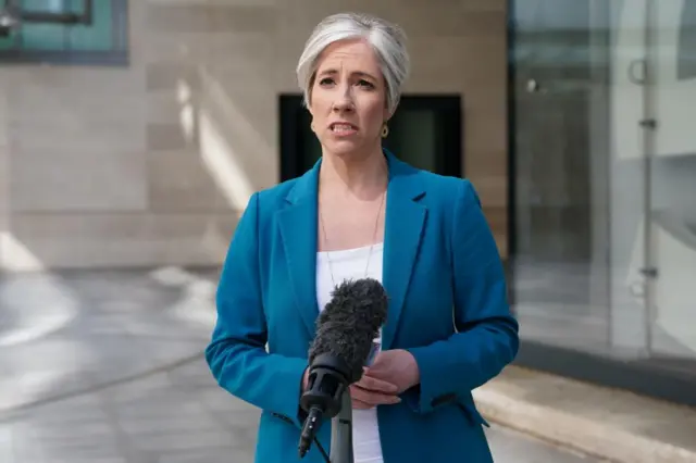 Liberal Democrat Deputy Leader Daisy Cooper wears a blue blazer and speaks behind a microphone outside.