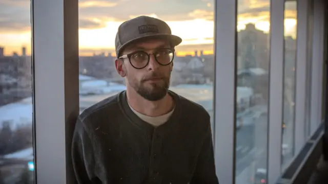 Brent Colman stands by a window as the sun sets behind him.