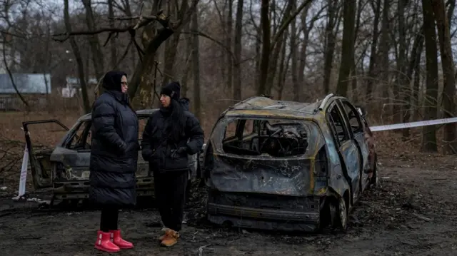 Two people stand near two burnt out cars in Chernihiv after a Russian drone strike