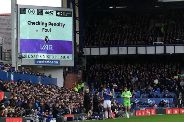 The big screen displays news that the VAR (Video Assistant Referee) is reviewing a posible penalty to Everton,