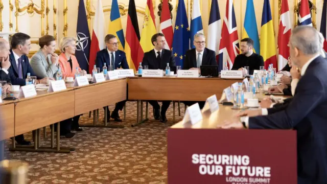 Keir Starmer and European leaders seated around a table at a summit in London. Starmer sits in between Macron and Zelensky.