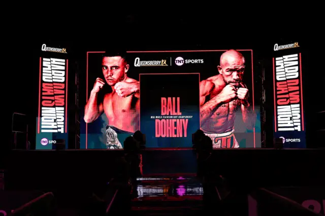 A large video screen showing Nick Ball and TJ Doheny with the writing 'Hard days night' at a boxing event in Liverpool