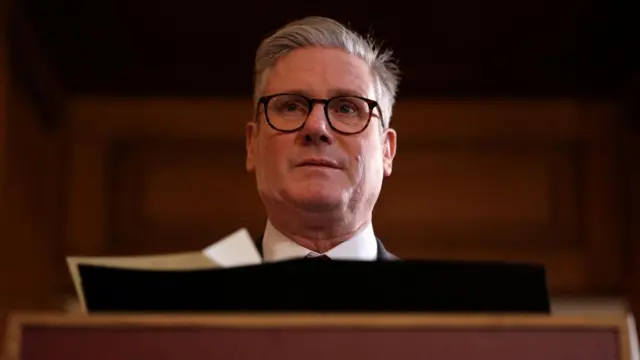 Starmer wears glasses and stands behind a podium.