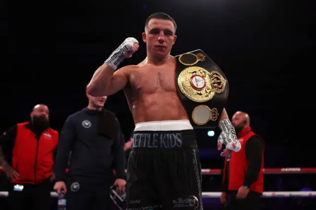 Nick Ball holds the WBA featherweight title over his shoulder in a boxing ring after beating Ronny Rios