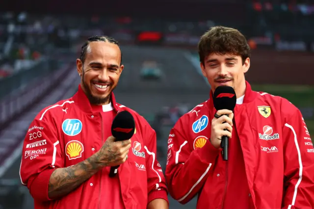 Lewis Hamilton and Charles Leclerc hold microphones in the fan zone