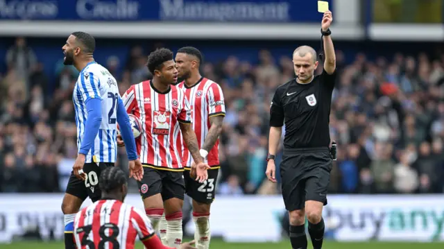 Femi Seriki is shown a yellow card by the referee